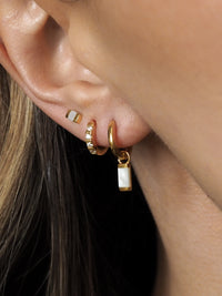 A model wearing multiple gold earrings layered together, featuring pearl pendant huggies, cubic zirconia huggies and mother of pearl studs.