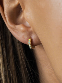 Close-up of a model wearing gold white opal huggies.