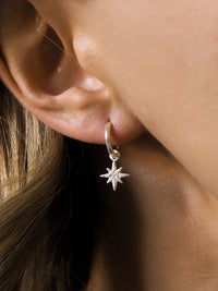 Close-up of a woman's ear wearing a sterling silver hoop earring with a delicate eight-pointed star pendant.