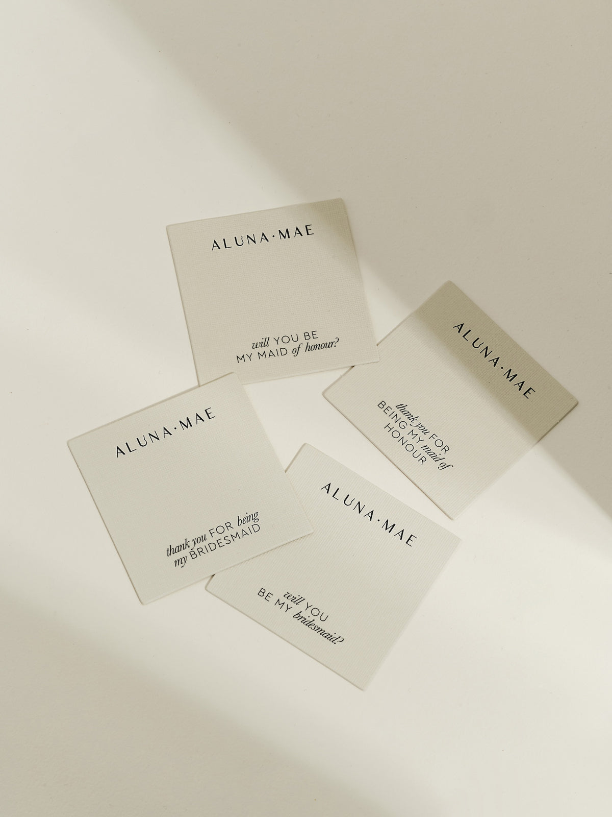 A flatlay of four Aluna Mae jewellery message cards with bridesmaid and maid of honour proposals and thank-you notes in elegant black text.