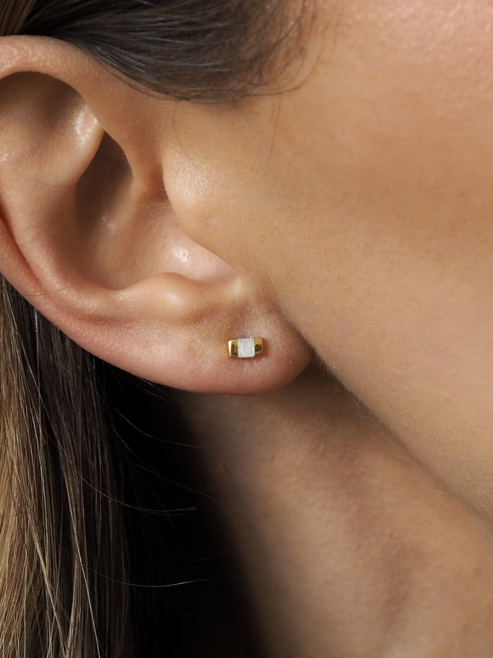 Close-up of a gold rectangular stud earring with a mother of pearl inlay worn on an ear.