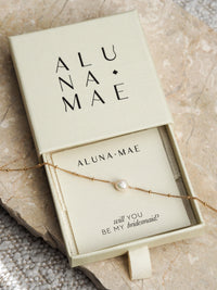 Gold chain bracelet with a single freshwater pearl in an Aluna Mae gift box featuring a "will you be my bridesmaid?" message card.