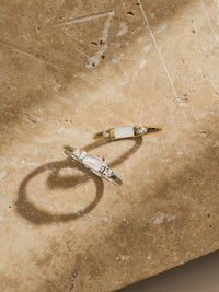 Two Aluna Mae rings displayed on travertine stone—one gold and one silver, each featuring a rectangular mother of pearl centre set between two cubic zirconia stones.