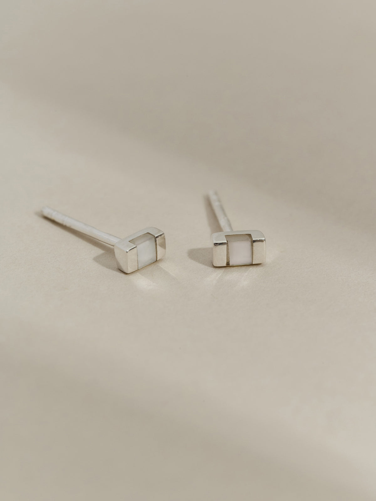 Pair of rectangular silver stud earrings with mother of pearl inlays, displayed on a neutral background.