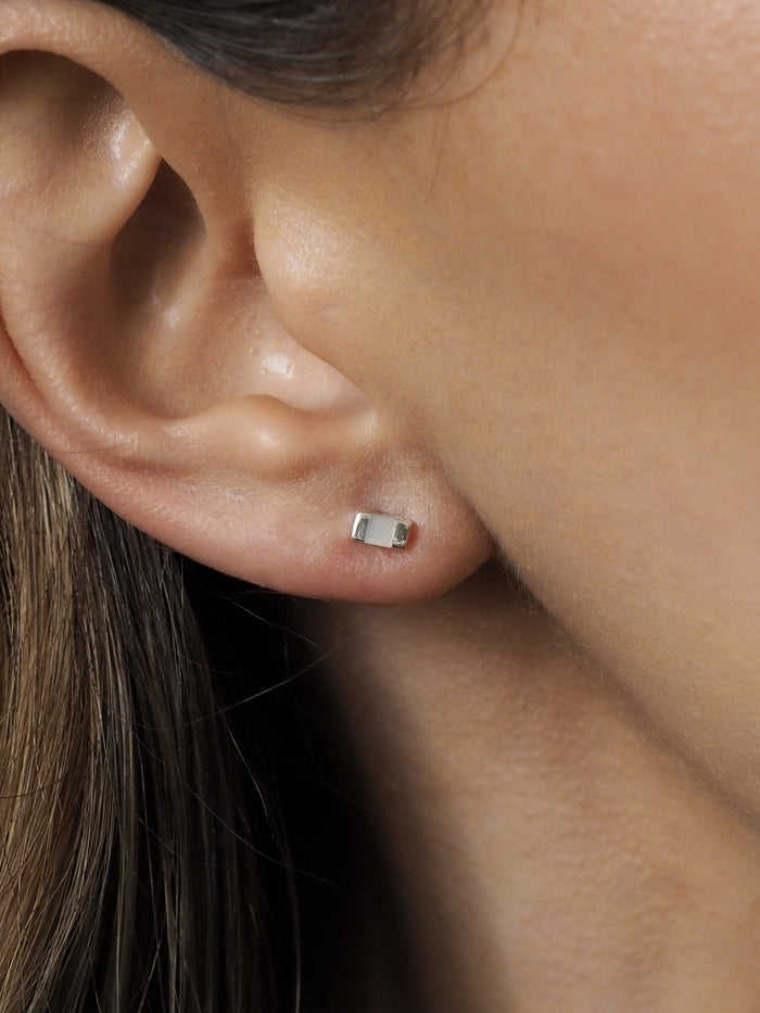 Close-up of a silver rectangular stud earring with a mother of pearl inlay, worn on a woman's ear.