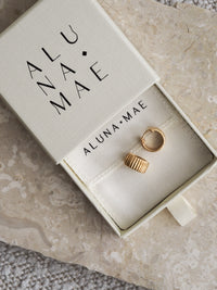 Ridged gold chunky hoop earrings displayed inside an Aluna Mae jewellery box, placed on a marble surface.
