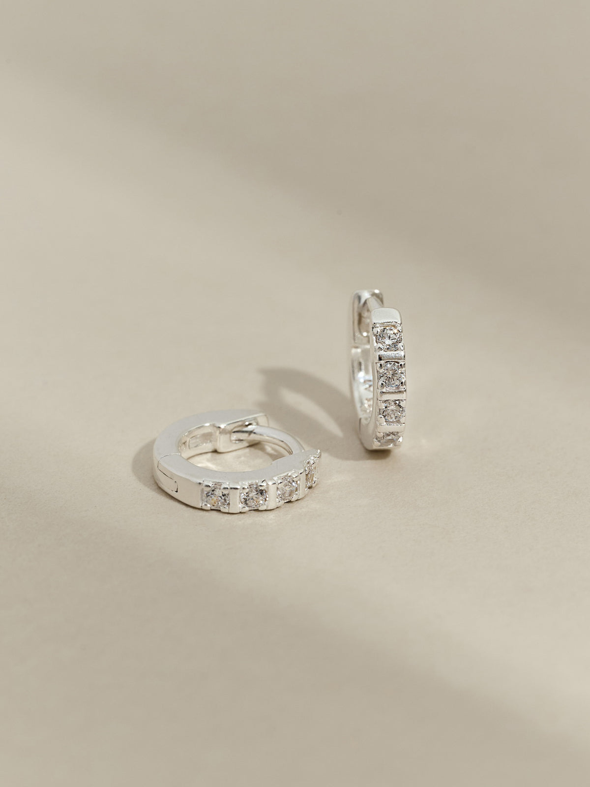 Pair of sterling silver huggie earrings with a row of cubic zirconia stones, displayed on a neutral background.