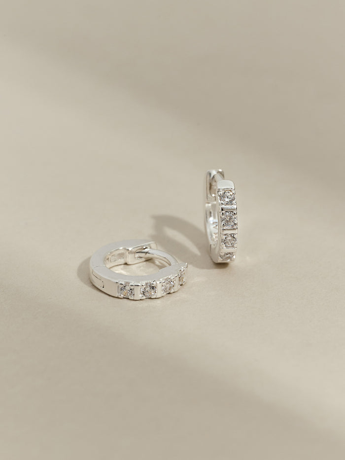 Pair of sterling silver huggie earrings with a row of cubic zirconia stones, displayed on a neutral background.