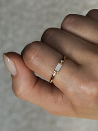 Gold vermeil ring with a mother of pearl centre stone and two cubic zirconia details, shown worn on a hand.