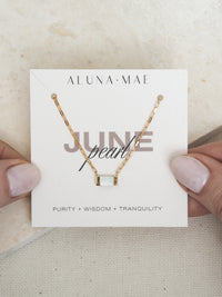 June birthstone necklace by Aluna Mae, featuring a rectangular mother of pearl pendant on a gold box chain, displayed on a card with gemstone meaning.