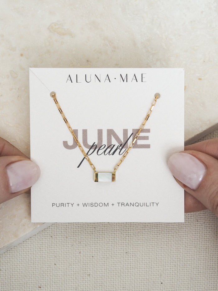 June birthstone necklace by Aluna Mae, featuring a rectangular mother of pearl pendant on a gold box chain, displayed on a card with gemstone meaning.
