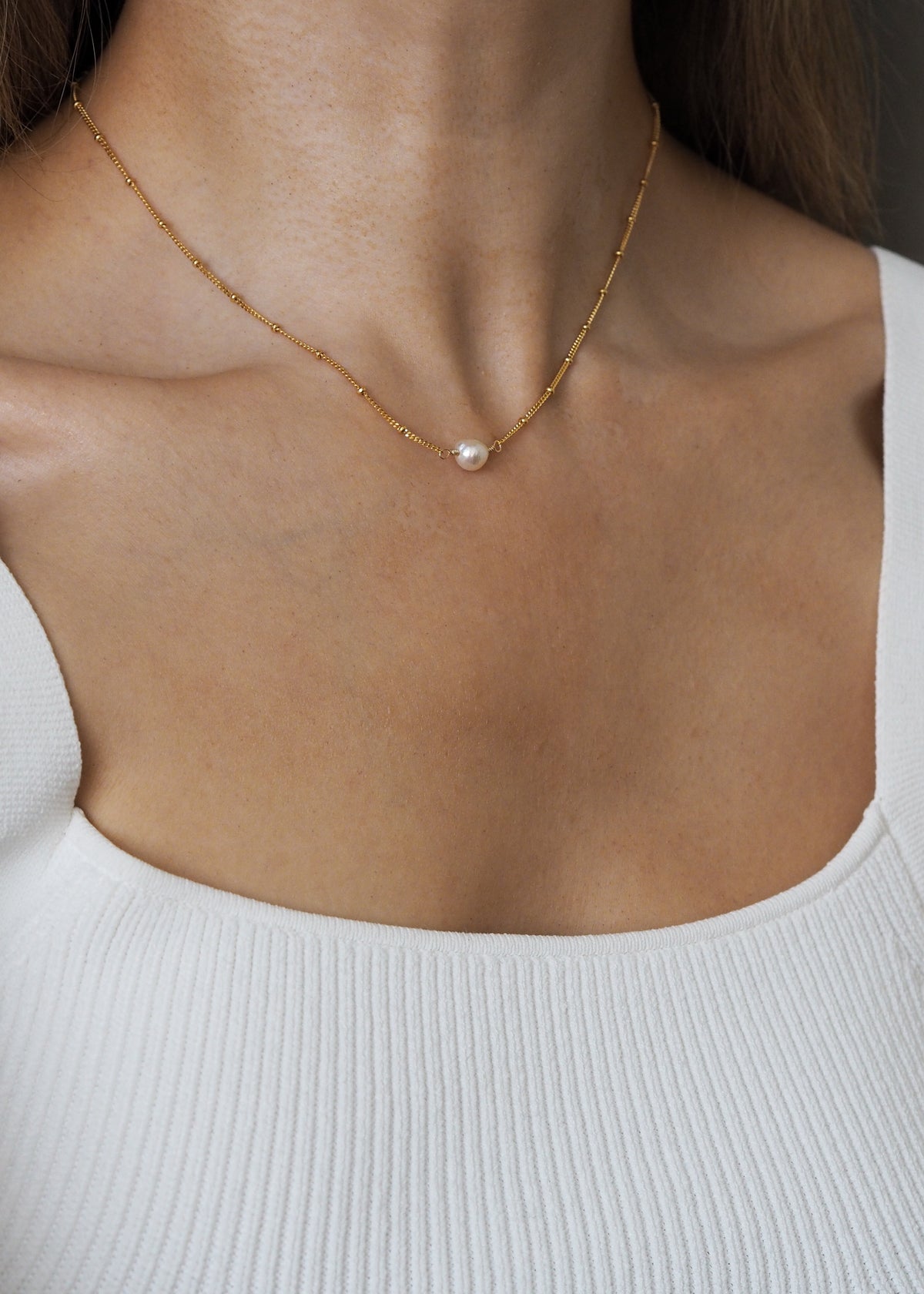 June birthstone necklace featuring a single freshwater pearl on an 18ct gold plated sterling silver satellite chain, worn on a model with a white ribbed square-neck top.