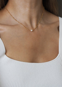 June birthstone necklace featuring a single freshwater pearl on an 18ct gold plated sterling silver satellite chain, worn on a model with a white ribbed square-neck top.