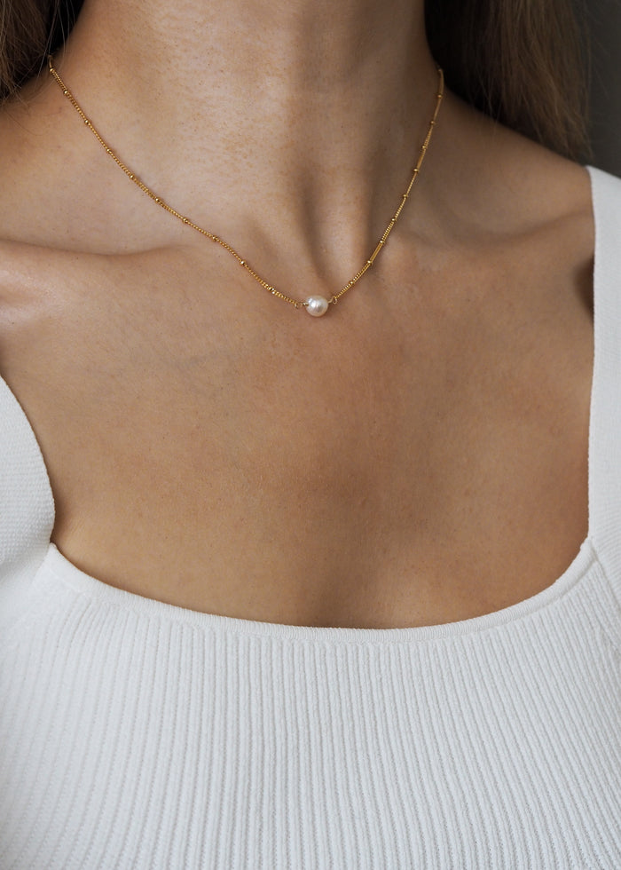 June birthstone necklace featuring a single freshwater pearl on an 18ct gold plated sterling silver satellite chain, worn on a model with a white ribbed square-neck top.