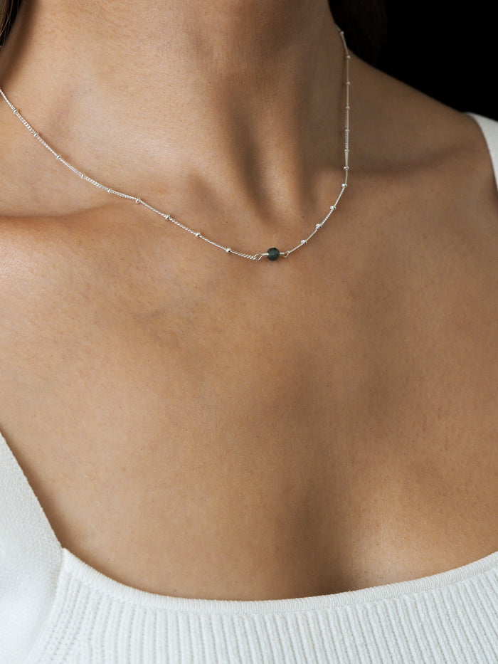 Close-up of a model wearing a May birthstone necklace with a green emerald gemstone, on a delicate sterling silver satellite chain.