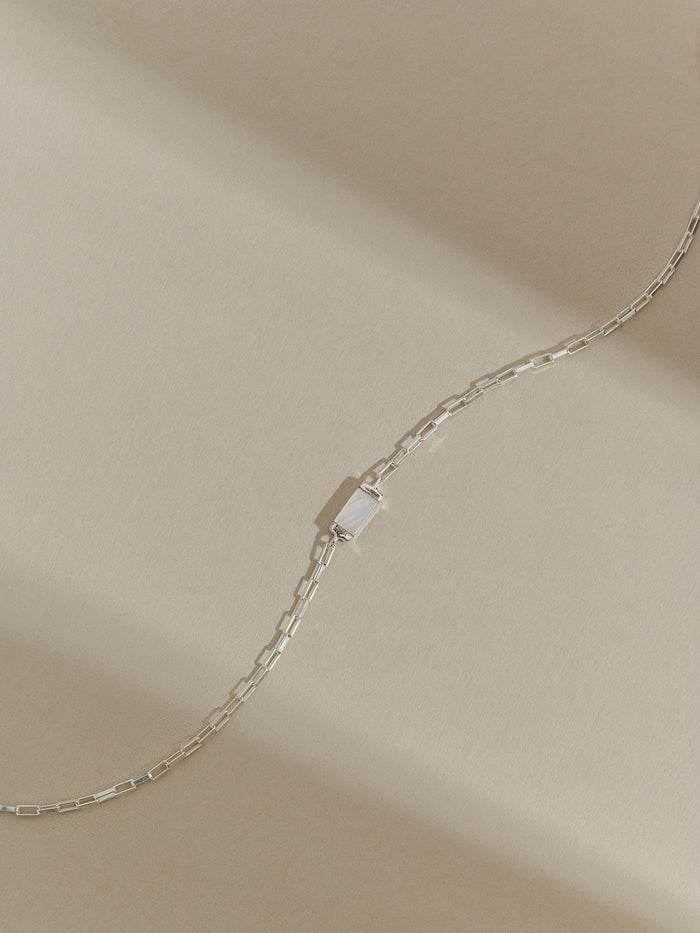Sterling silver box chain bracelet with a rectangular mother of pearl pendant, displayed on a soft neutral background with natural shadows.