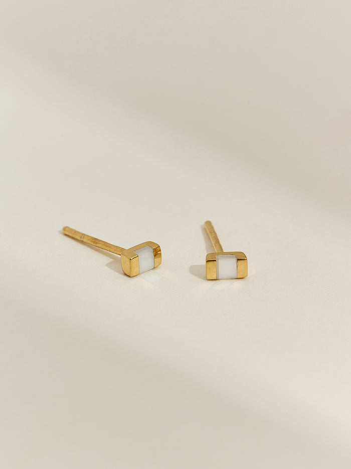 Close-up of a gold rectangular stud earring with a mother of pearl inlay worn on an ear.