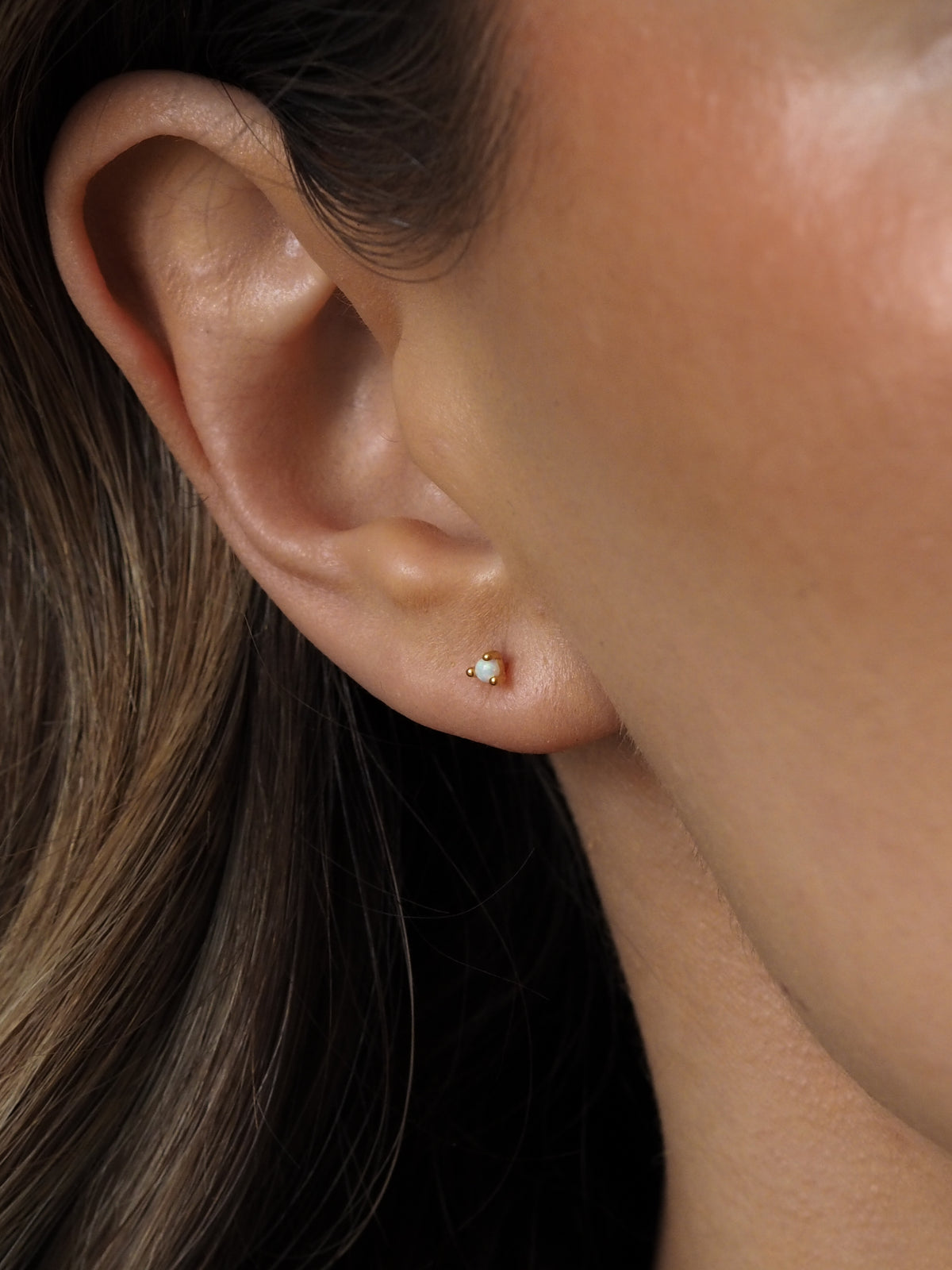Close-up of a model's ear wearing an October birthstone opal gemstone stud earring, set in 18ct gold-plated sterling silver.