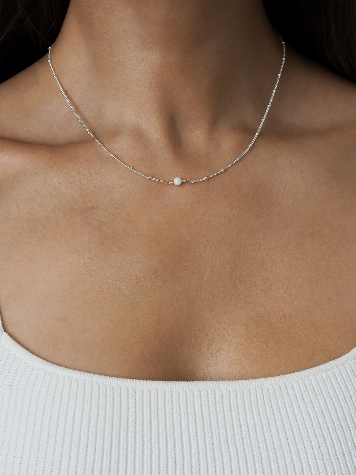 Close-up of sterling silver satellite chain necklace with October white opal pendant, styled with a white ribbed top