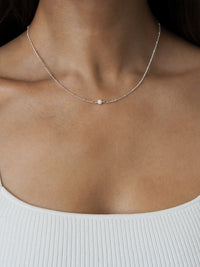 Close-up of sterling silver satellite chain necklace with October white opal pendant, styled with a white ribbed top