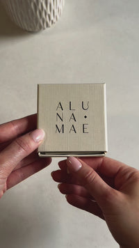 A hand opens an Aluna Mae jewellery gift box to reveal a bridesmaid message card inside.