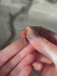 Close-up of a hand holding a gold-plated star pendant earring with a central opal and cubic zirconia detailing, shown in natural light.