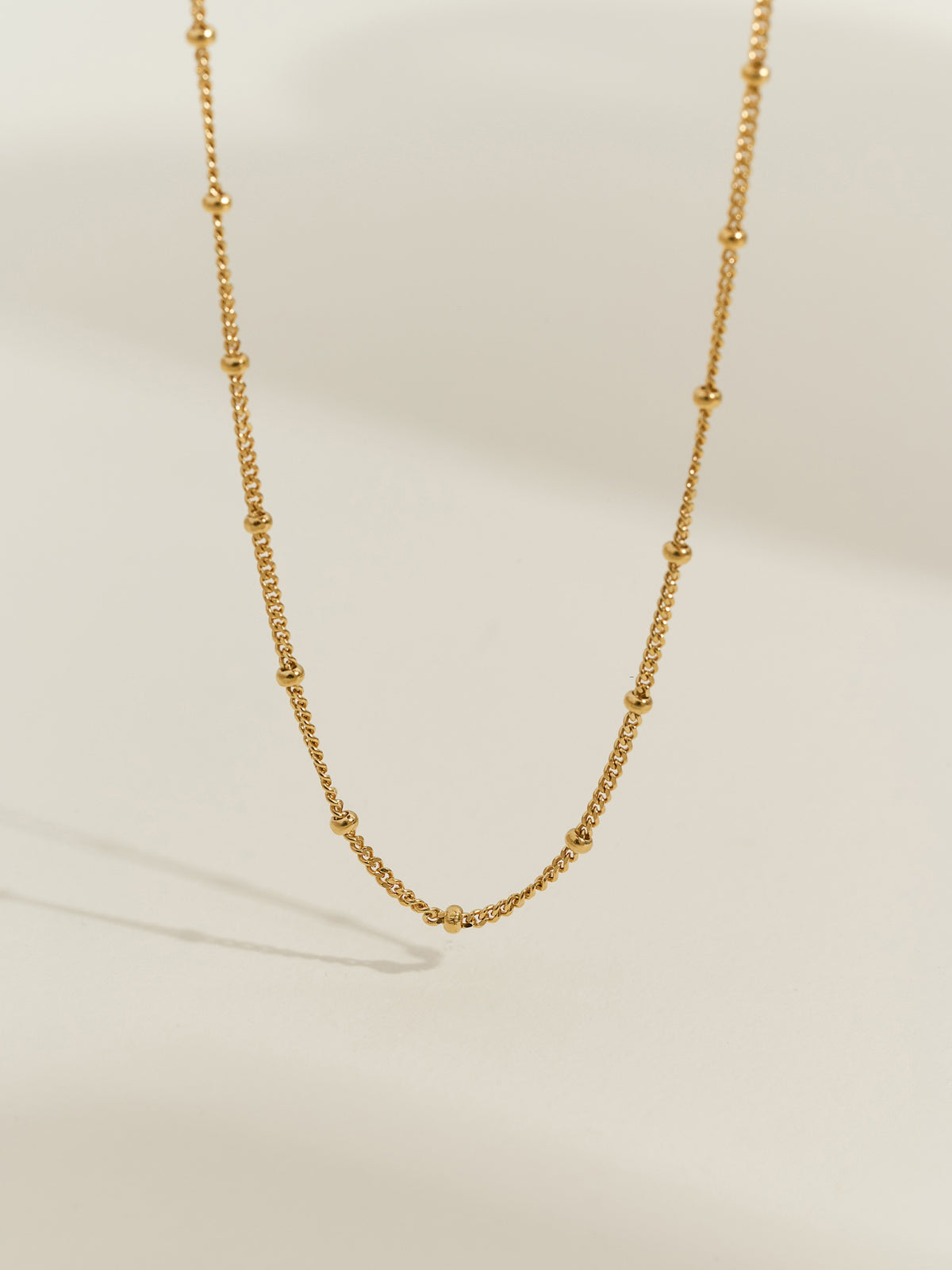 Close-up of a gold-plated satellite chain necklace, featuring evenly spaced tiny gold beads on a delicate chain.