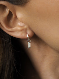 Sterling silver hoop earring worn in ear, featuring a rectangular mother of pearl drop charm.