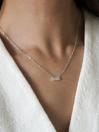 Sterling silver necklace featuring a rectangular mother of pearl pendant, worn with a white textured fabric top.