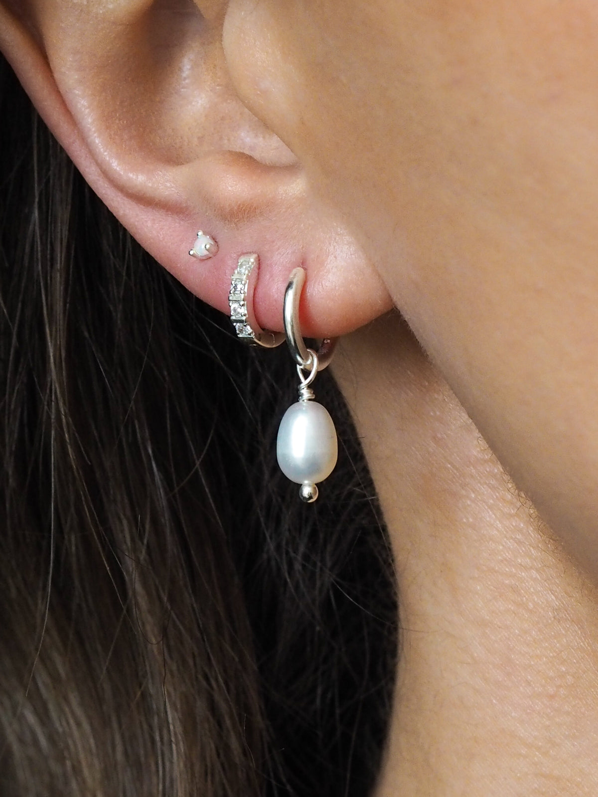 Sterling silver freshwater pearl drop earring styled with a dainty opal stud and a cubic zirconia huggie on the same ear.