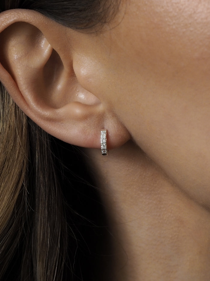 Sterling silver huggie earring with cubic zirconia stones, worn on a model’s ear.