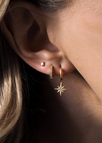 A model wearing multiple gold earrings layered together, featuring star hoops, opal studs and huggie details.
