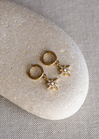A pair of gold-plated huggie earrings with star-shaped opal and cubic zirconia charms, displayed on a smooth neutral-toned stone surface.