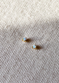 Pair of October birthstone opal gemstone stud earrings set in 18ct gold-plated sterling silver, displayed on a textured cream fabric background.
