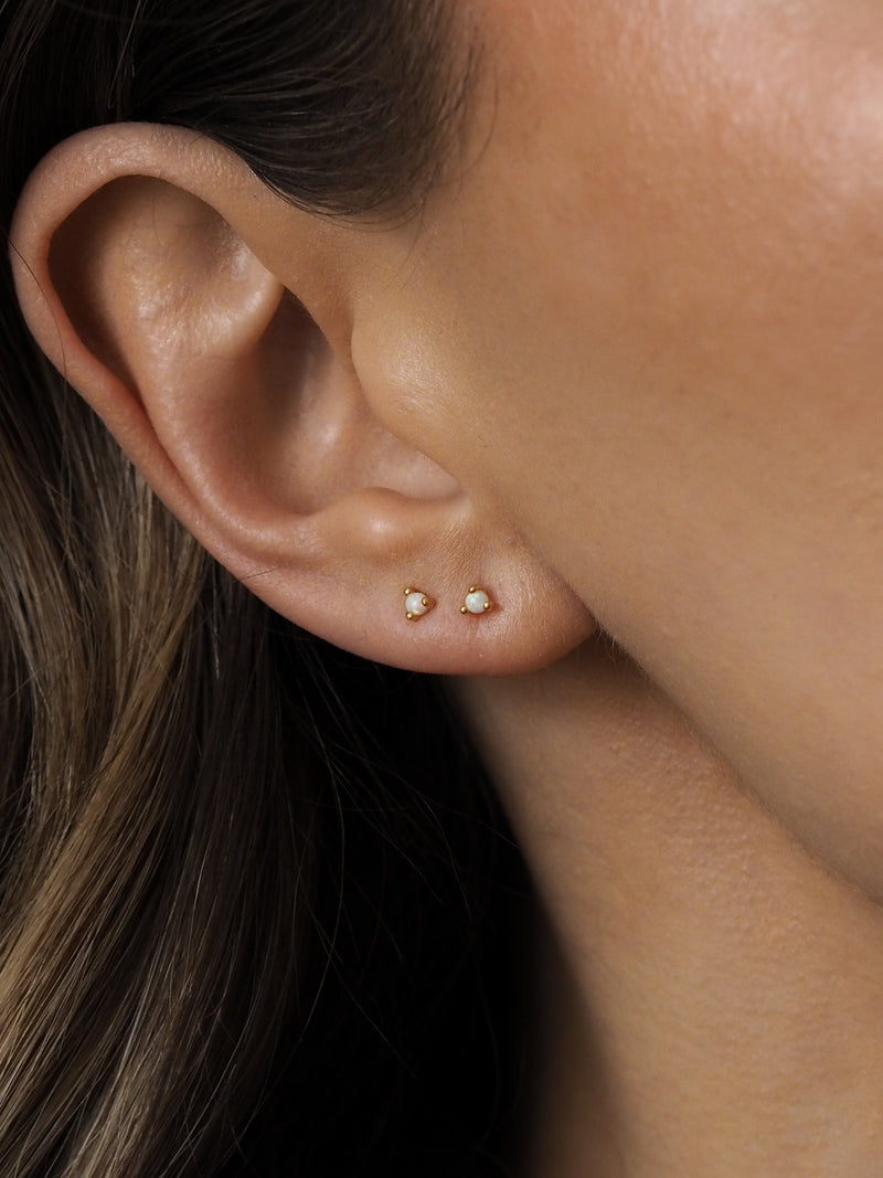 A model wearing two delicate gold white opal stud earrings, layered together on one ear.