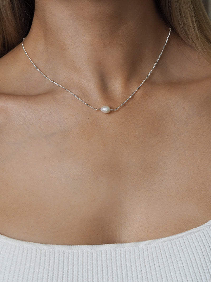 Freshwater pearl necklace with a sterling silver satellite chain, worn by a model in a white ribbed top.
