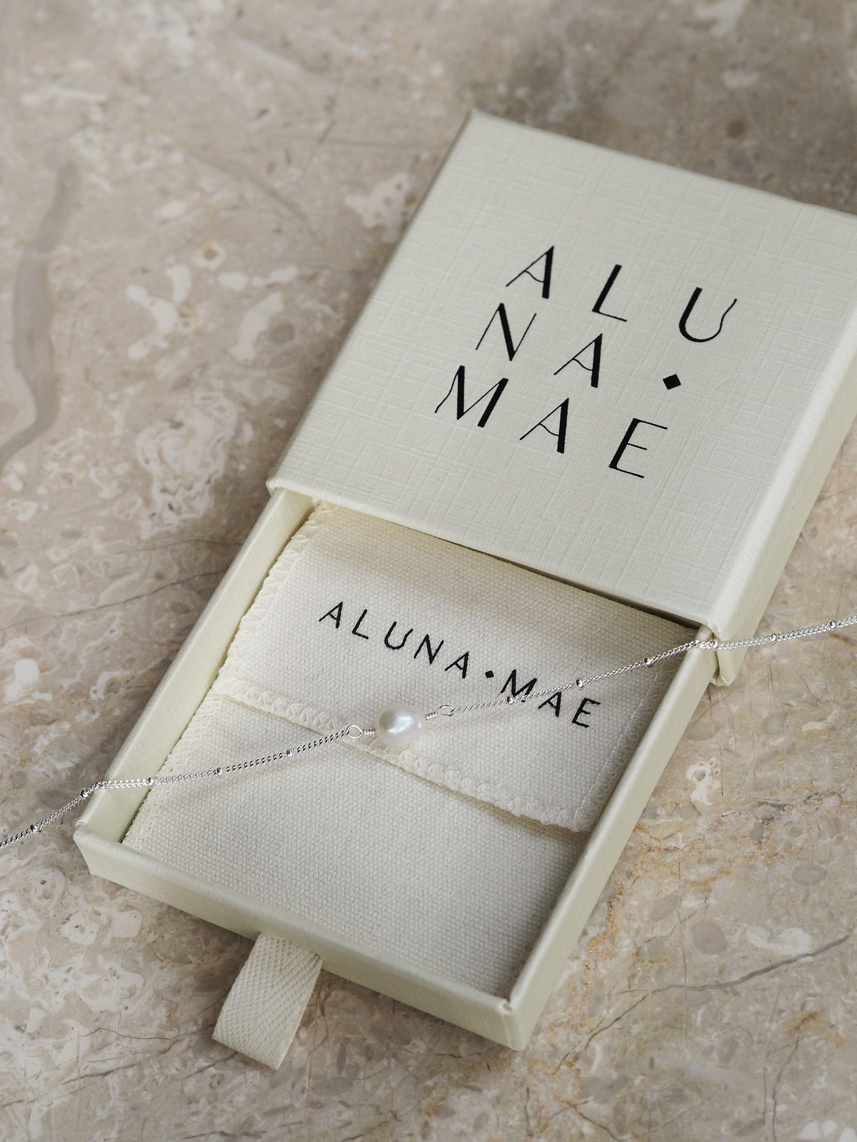 Close-up of a sterling silver freshwater pearl satellite chain bracelet, displayed with an Aluna Mae gift box.