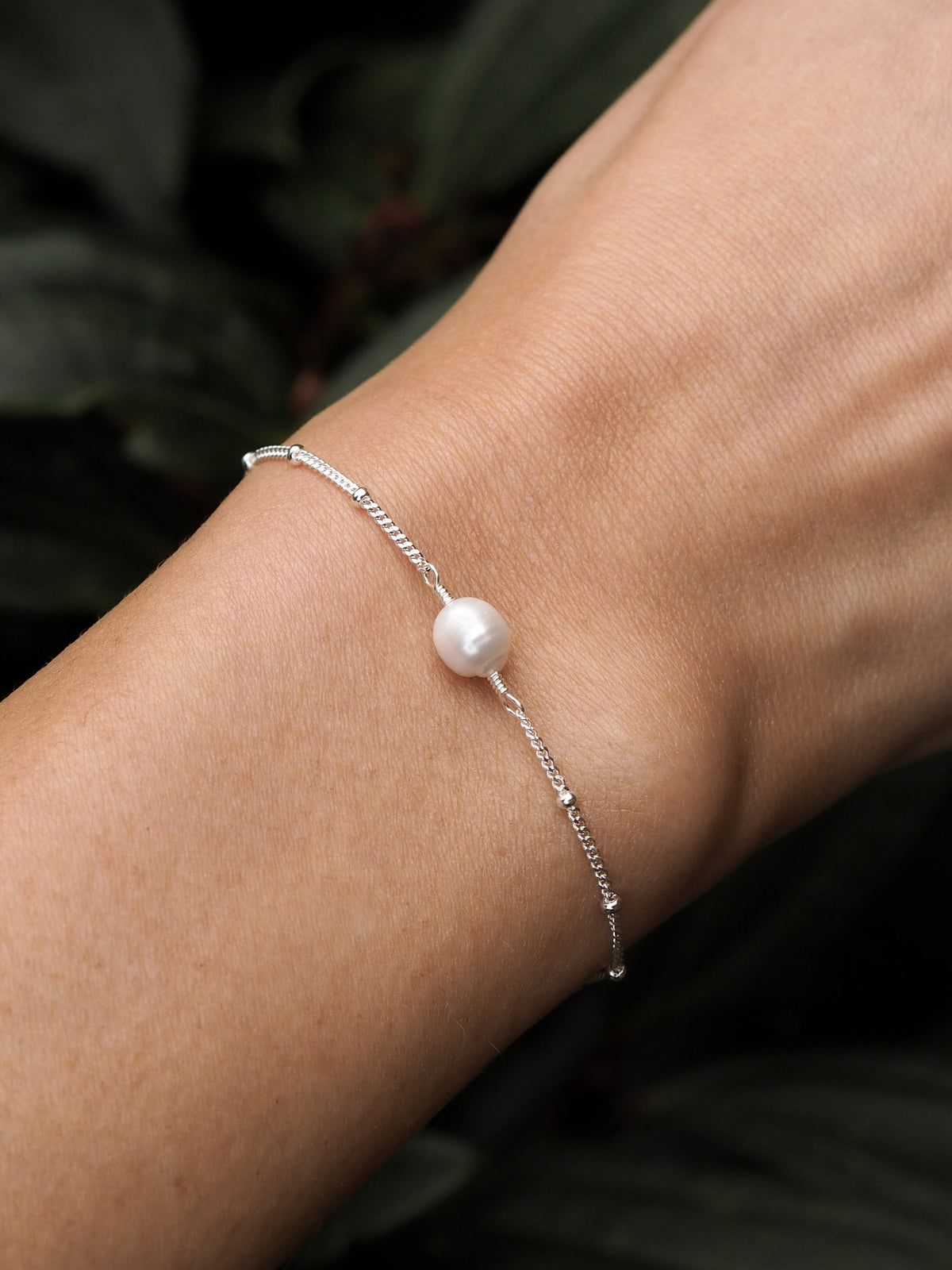 Close-up of a model wearing a sterling silver freshwater pearl satellite chain bracelet. 