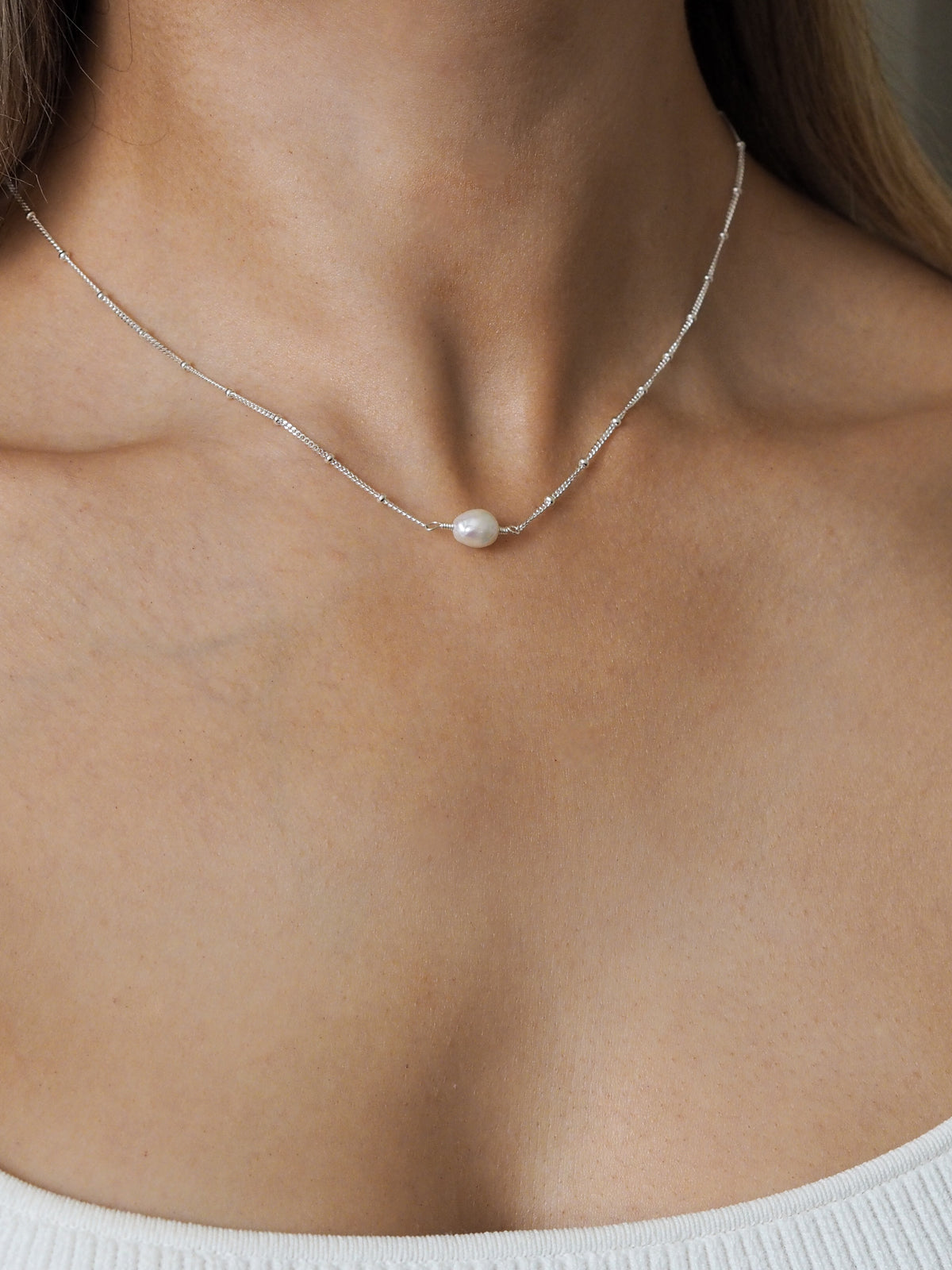 Close-up of a model wearing a sterling silver freshwater pearl satellite chain necklace.