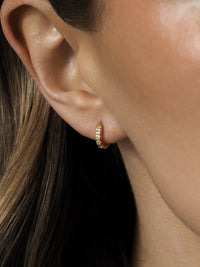 Close-up of a model wearing gold cubic zirconia huggies. 