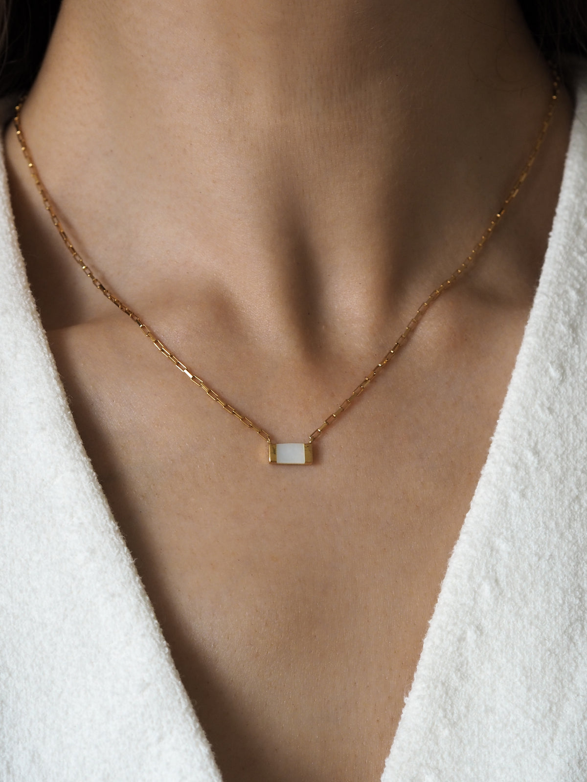 A model wearing a gold box chain necklace with a mother of pearl gemstone.