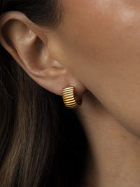 A model wearing bold chunky gold hoop earrings with ribbed detail.