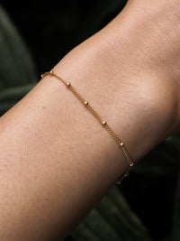 Close-up of a model wearing a minimal gold satellite chain bracelet. 