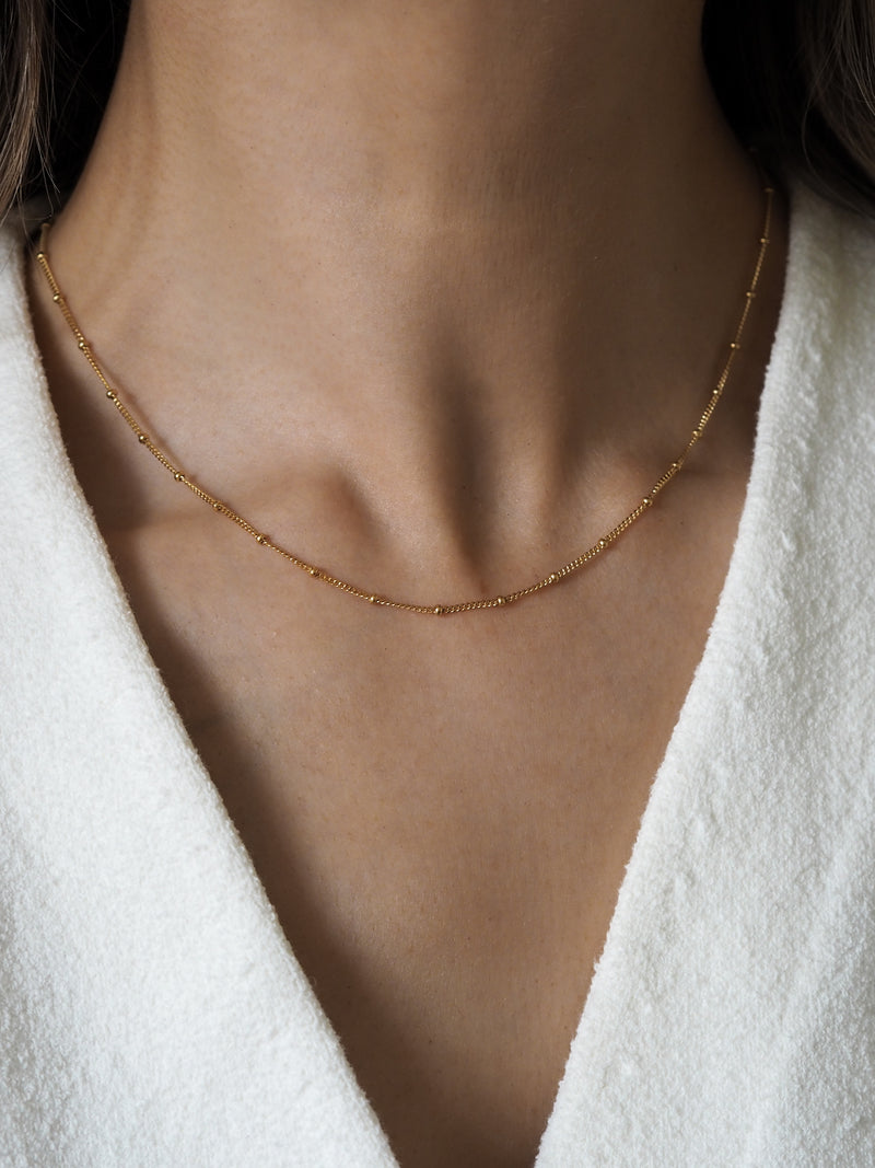 Close-up of a model wearing a minimal gold satellite chain necklace, creating an elegant and understated look.