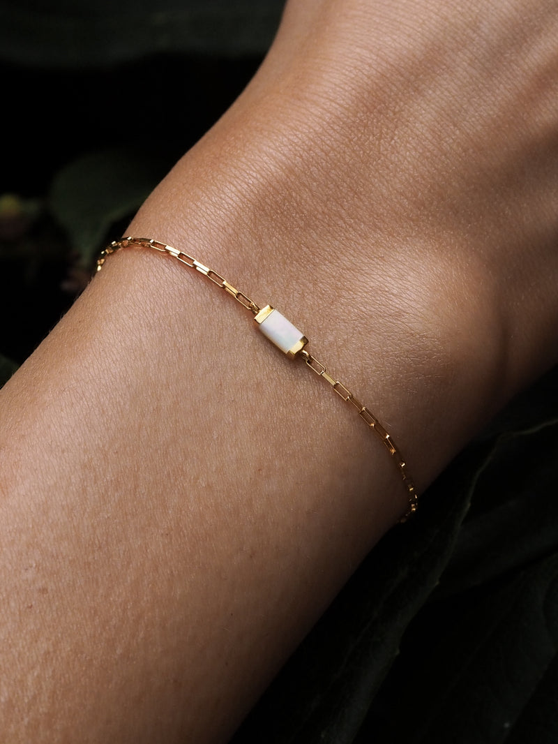 A model wearing a gold box chain bracelet with a mother of pearl gemstone.