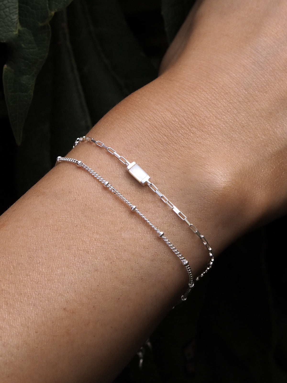 A model wearing layered sterling silver bracelets that feature mother of pearl accents and satellite chain details.