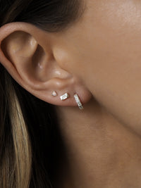 A model wearing multiple sterling silver earrings layered together, featuring cubic zirconia huggies, mother of pearl studs and opal studs.