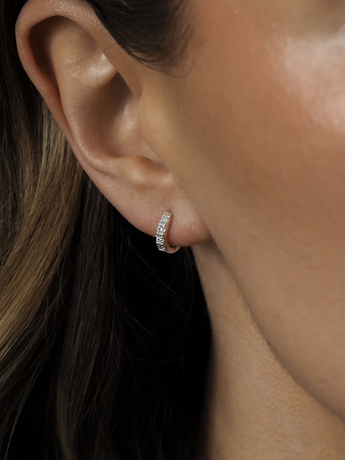 Close-up of a model wearing sterling silver cubic zirconia huggies. 