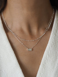 A model wearing multiple silver necklaces layered together, featuring elegant mother of pearl accents and satellite chain details.