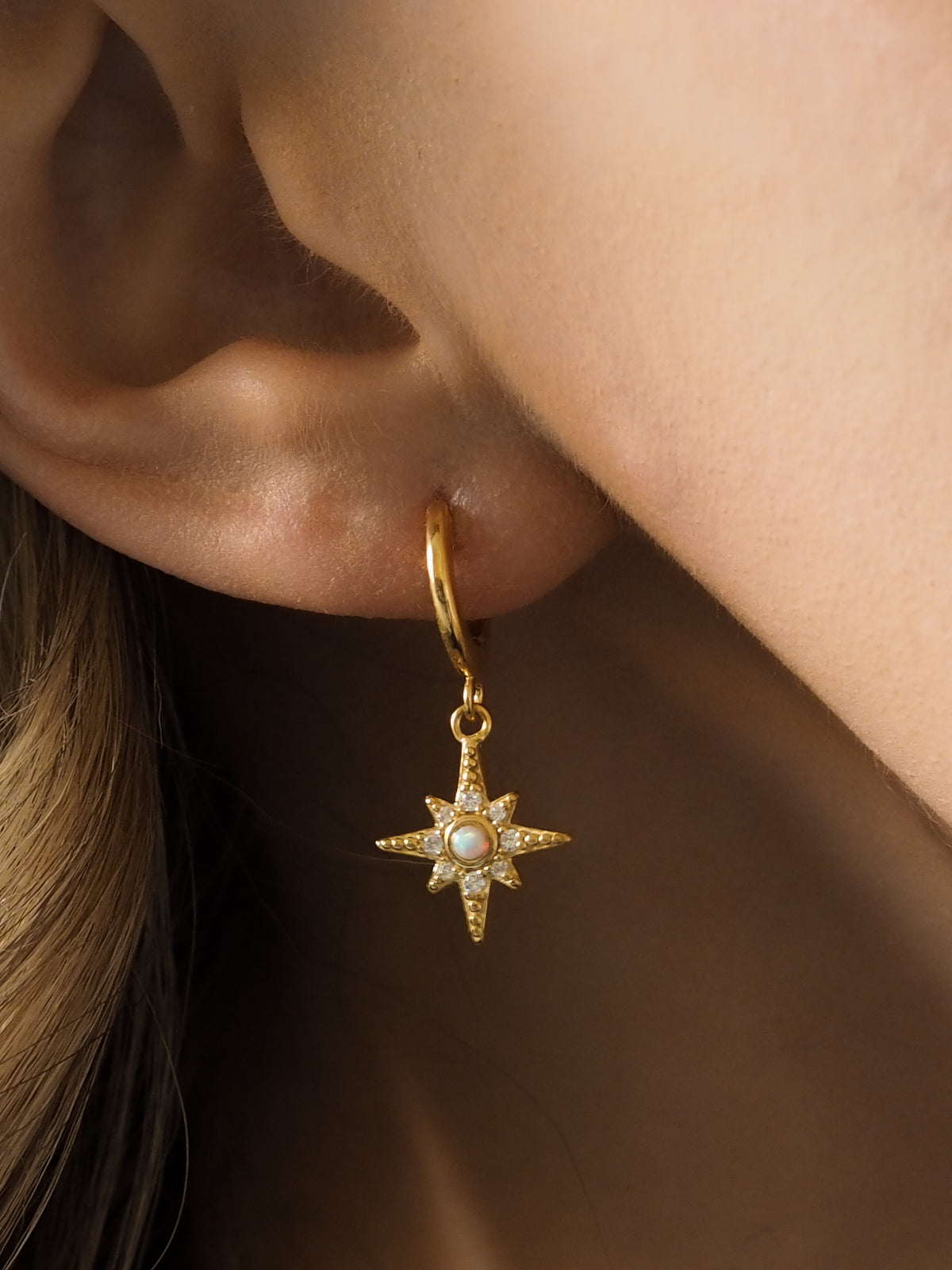 Close-up of a model wearing gold star pendant hoops with opal and cubic zirconia gemstones.